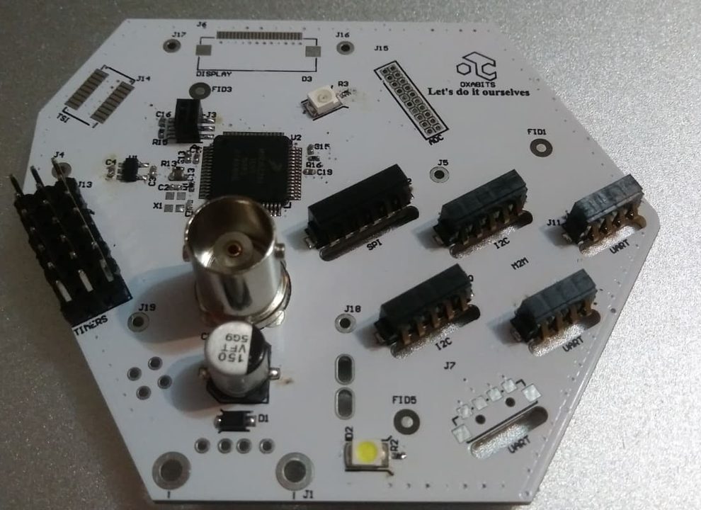 Placa electrónica hexagonal blanca diseñada por OXABITS, con microcontrolador, conector BNC y puertos SPI, I2C y UART